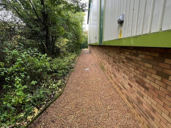 Gravel path beside metal building, trees on left.