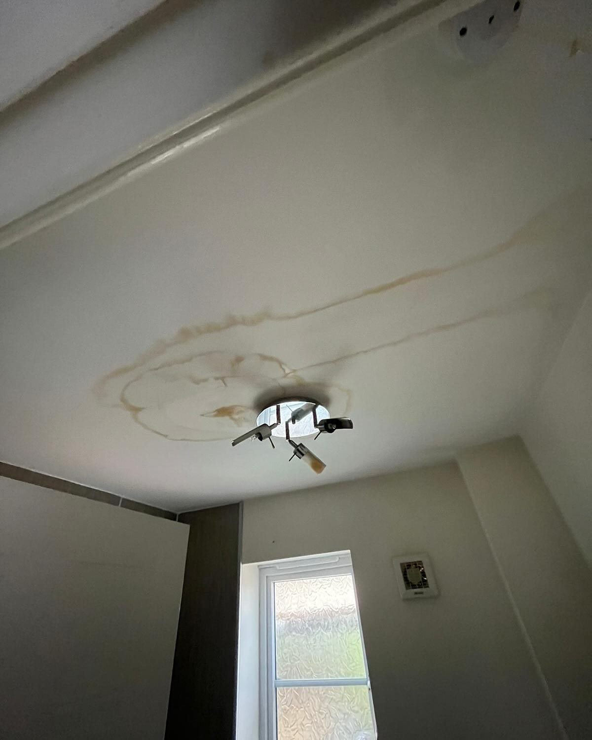 Ceiling water stain near light fixture indoors.